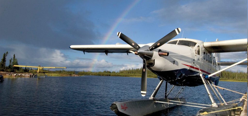 Portrait image of a float plane sitting in the water surrounded by blue skies and a rainbow