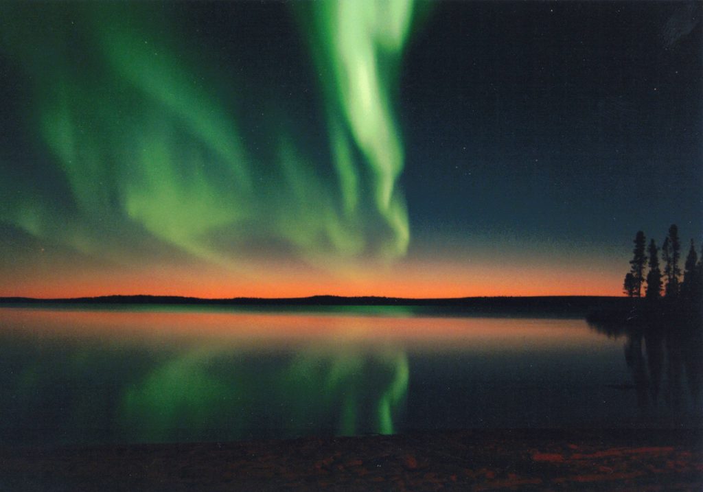 Canadian Northern Lights during a sunset with orange at the horizon, a dark starry night, and green streams of light