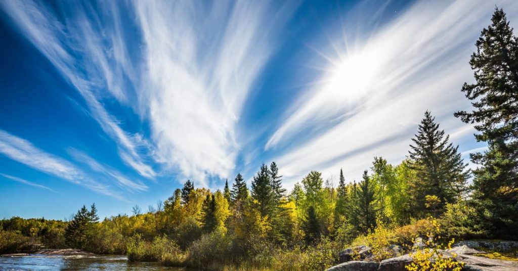 A beautiful river in Manitoba surrounded by green trees and massive rocks on a bright and sunny day.